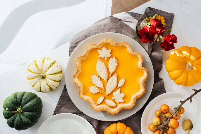 A beautifully styled pumpkin pie surrounded by autumn-themed decorations and mini pumpkins.